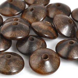May include: A group of brown wooden beads with a hole in the center of each bead. The beads are flat and have a slightly raised center.