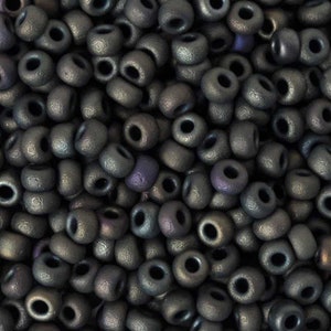 May include: Close-up of a pile of dark gray, metallic-looking beads. The beads are cylindrical with a hole running through the center. The surface of the beads has a textured appearance, and some show hints of purple and blue.