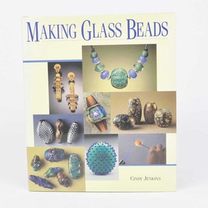 May include: A book titled "MAKING GLASS BEADS" with images of colorful glass beads, earrings, and a necklace. The cover features various bead designs, including oval, round, and patterned beads in shades of blue, green, gold, and black. The author's name, Cindy Jenkins, is also visible.