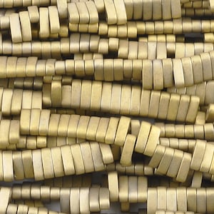May include: A close-up of a pile of gold-colored rectangular beads. The beads are made of a smooth, matte material and have a slightly rounded edge.
