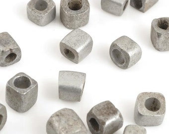 May include: A collection of silver metal beads with a square shape and a hole in the center. The beads are scattered on a white surface.