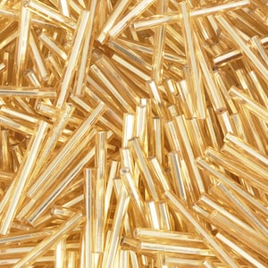 May include: A close-up shot of a pile of golden, cylindrical beads. The beads are translucent and have a slightly iridescent quality, catching the light. They are scattered in a random pattern, creating a textured surface.