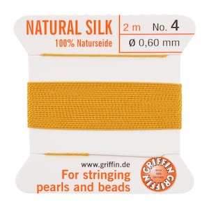 May include: A spool of natural silk thread, color mustard yellow, for stringing pearls and beads. The spool is white with orange text that reads "NATURAL SILK" and "For stringing pearls and beads". The thread is 2 meters long and 0.60 mm in diameter.