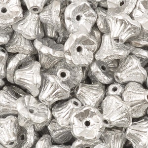 May include: A pile of silver metal flower-shaped beads. The beads have a textured surface and a small hole in the center.
