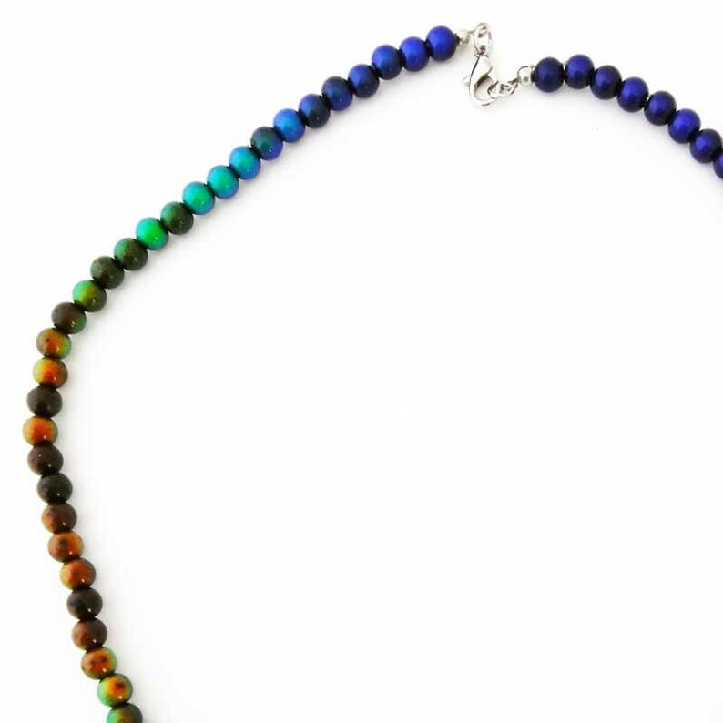 May include: A beaded necklace with a gradient of colors, transitioning from brown to green, teal, blue, and finally dark blue. The necklace features a silver clasp and is displayed against a white background. The beads are round and evenly spaced.