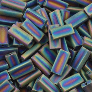 May include: A close-up of a pile of iridescent green, blue, and purple glass beads. The beads are rectangular in shape and have a smooth, polished finish.