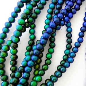 May include: Strands of round beads in shades of blue and green. The beads have a glossy finish and are strung together, creating a textured and colorful pattern. The beads are likely used for jewelry making.