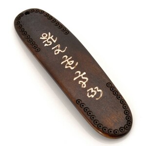 K&ouml;nnte beinhalten: Ein dunkelbraunes Holz Lesezeichen mit einer goldenen Inschrift in koreanischer Schrift. Das Lesezeichen hat einen dekorativen Rand aus kleinen Kreisen.