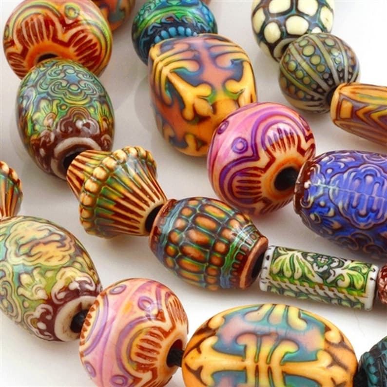 May include: A selection of vibrant, patterned beads in diverse shapes. The beads showcase intricate designs in orange, yellow, pink, green, and blue. Some beads have a glossy finish, while others have a more matte appearance.