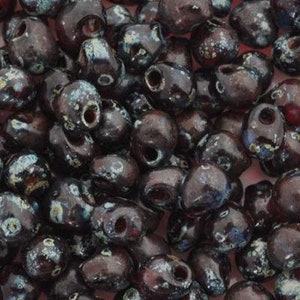May include: A close-up of a pile of dark purple glass beads with a speckled white and silver design. The beads are small and round, with a hole in the center.