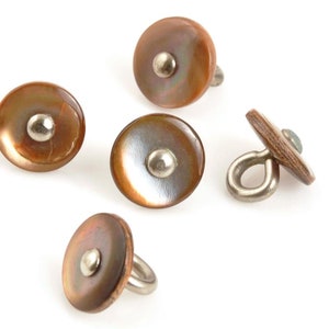 May include: Five brown shell buttons with a silver-colored metal shank. The buttons have a circular shape with a central silver-colored metal stud. The shell has a pearlescent sheen, with colors ranging from light brown to dark brown.