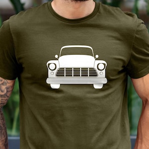 Op de afbeelding: Olijfgroen t-shirt met een witte afbeelding van een klassieke auto. Het autodesign omvat koplampen, een grille en een bumper. Het shirt is gemaakt van een zacht materiaal en heeft korte mouwen.
