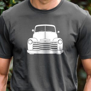 May include: Dark grey t-shirt with a white outline of a classic pickup truck design. The graphic is positioned centrally on the chest. The shirt is made of a soft fabric and has short sleeves.