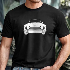 Puede incluir: Camiseta negra con un dibujo lineal blanco de un coche descapotable cl&aacute;sico. El coche tiene faros redondos y un parachoques delantero prominente. El dise&ntilde;o est&aacute; centrado en la camiseta, ofreciendo una est&eacute;tica limpia y minimalista. La camiseta es de material suave.