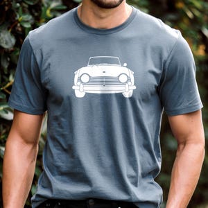 Puede incluir: Una camiseta gris pizarra con un gr&aacute;fico blanco de un coche descapotable cl&aacute;sico. Los faros, la parrilla y el parabrisas del coche son visibles. La camiseta es de material suave y tiene mangas cortas.