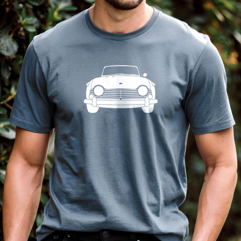 Puede incluir: Una camiseta gris pizarra con un gr&aacute;fico blanco de un coche descapotable cl&aacute;sico. Los faros, la parrilla y el parabrisas del coche son visibles. La camiseta es de material suave y tiene mangas cortas.
