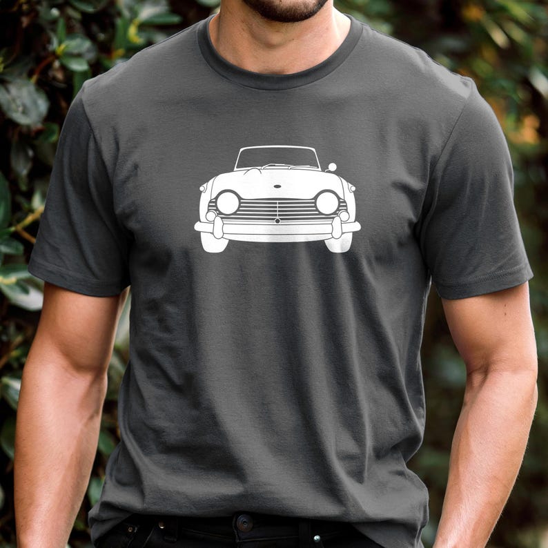 Puede incluir: Camiseta gris oscuro con un contorno blanco de un coche descapotable cl&aacute;sico. Se muestra la vista frontal del coche, con faros, parrilla y parabrisas. La camiseta est&aacute; hecha de un material suave.