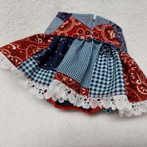 May include: A patchwork baby skirt with a red, white, and blue bandana print. The skirt has a white lace trim and is gathered at the waist.