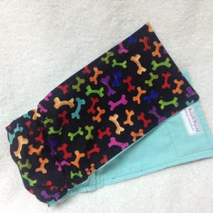 May include: A black and turquoise reusable cloth diaper with a colorful bone print. The diaper has a white tag with the text "Little Puppy" on it.