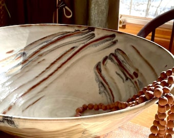 May include: A large white ceramic bowl with brown and gray marbling. The bowl is sitting on a wooden surface and has a strand of brown beads inside.