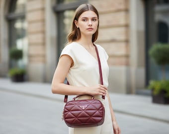 May include: A burgundy quilted crossbody bag with a silver chain strap and top handle. The bag features a geometric pattern and a silver logo on the front. The bag is worn over the shoulder.