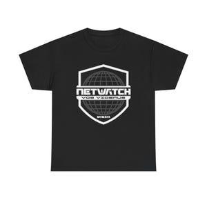 May include: A black short-sleeve t-shirt featuring a white shield-shaped graphic on the chest. The design includes a globe icon, the text NETWATCH, the Latin phrase VOS VIDEMUS, and the Roman numeral MCMXCI centered within the shield outline.