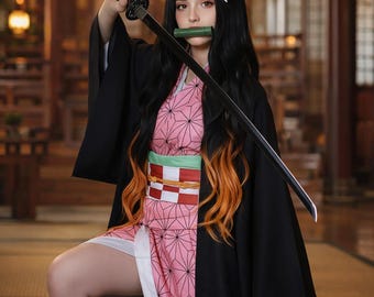 Puede incluir: Un disfraz de personaje que incluye un kimono rosa con estampado de hojas de cáñamo negro, una chaqueta haori negra, una boquilla de bambú verde y una espada katana negra. El conjunto incluye un cinturón obi a cuadros rojos y blancos y polainas negras.