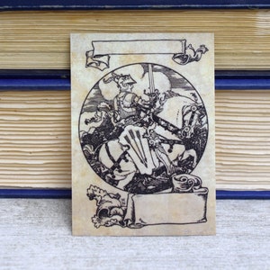 May include: A black and white illustration of a knight on horseback riding into battle. The knight is wearing armour and holding a sword. The horse is rearing up on its hind legs. The illustration is surrounded by a decorative border.