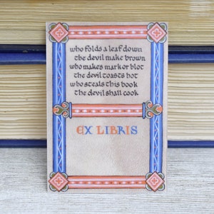 Pode incluir: Um ex libris com uma borda decorativa em tons de azul, laranja e branco. O texto diz: "Quem dobra uma folha para baixo o diabo faz marrom quem faz uma marca ou uma mancha o diabo torra quente quem rouba este livro o diabo vai cozinhar" e "Ex Libris".