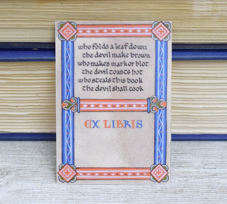 Pode incluir: Um ex libris com uma borda decorativa em tons de azul, laranja e branco. O texto diz: "Quem dobra uma folha para baixo o diabo faz marrom quem faz uma marca ou uma mancha o diabo torra quente quem rouba este livro o diabo vai cozinhar" e "Ex Libris".