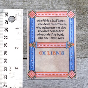 Pode incluir: Um ex libris com uma borda decorativa em tons de azul, laranja e vermelho. O texto diz: "who folds a leaf down the devil make brown who makes mark or blot the devil toasts hot whos steals this book the devil shall cook" e "EX LIBRIS".