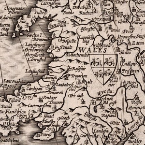 Peut inclure: Une carte ancienne du Pays de Galles, montrant les principales villes et villages du pays. La carte est en noir et blanc et pr&eacute;sente un blason au centre.