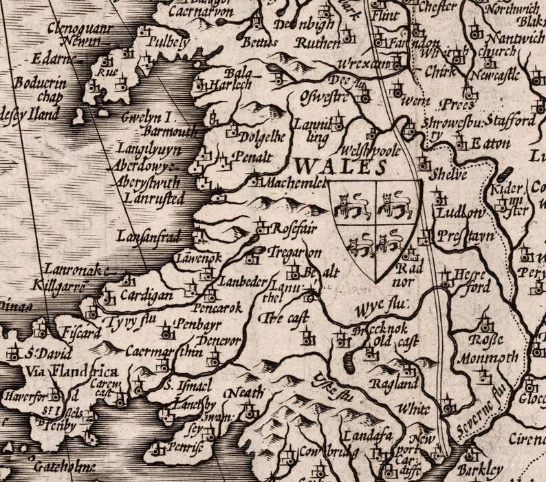 Peut inclure: Une carte ancienne du Pays de Galles, montrant les principales villes et villages du pays. La carte est en noir et blanc et pr&eacute;sente un blason au centre.