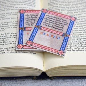 Pode incluir: Dois ex libris decorativos com uma borda vermelha e azul. Os ex libris apresentam um design de estilo medieval com um fundo branco e texto preto. O texto nos ex libris diz "who folds a leaf down the devil make brown who makes markor bloc the devil coasts bot whosceals this book the devil shall cook" e "EX LIBRIS".