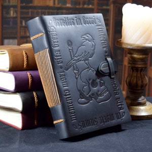 The black leather journal stands upright against a stack of other books. A candle and bookshelves are seen in the background.
