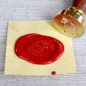 Könnte beinhalten: Ein rotes Siegelwachs mit einem detaillierten Wolfskopfdesign, geprägt mit einem Stempel aus Messing. Der Stempel ist im Hintergrund sichtbar.