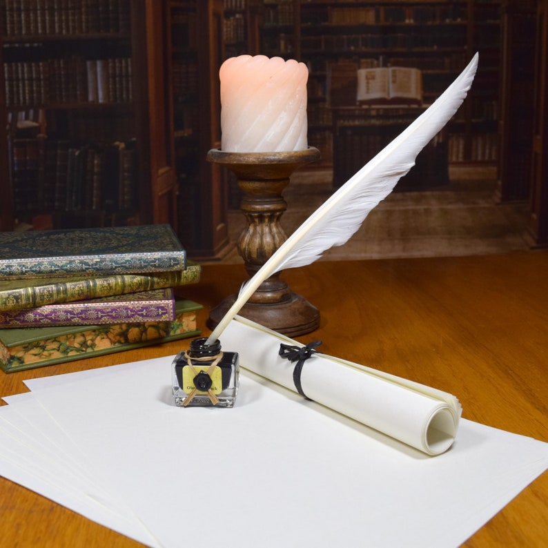 Feather quill in ink bottle, with a roll of paper, on a desk in front of a candle and stack of books