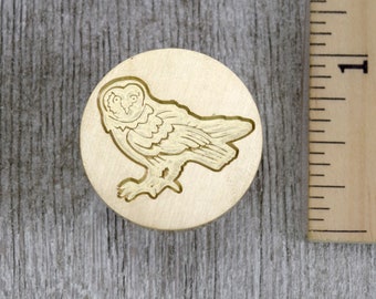 Puede incluir: Un sello de latón con un diseño detallado de un búho mirando hacia la izquierda. El búho tiene una cabeza redonda con ojos grandes y un patrón de ala detallado.