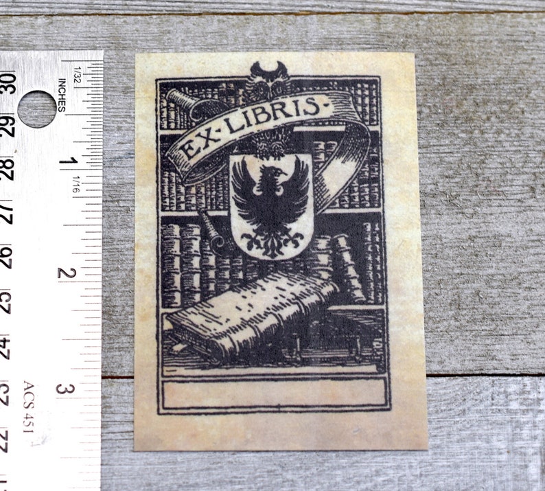 K&ouml;nnte beinhalten: Eine Schwarzwei&szlig;illustration eines Exlibris mit einem Wappen, das einen Vogel mit ausgebreiteten Fl&uuml;geln zeigt. Das Wappen ist von einem Banner mit dem Text "EX-LIBRIS" umgeben und vor einem Hintergrund von B&uuml;cherregalen mit B&uuml;chern platziert. Das Exlibris hat einen leeren Platz f&uuml;r einen Namen oder eine Inschrift.