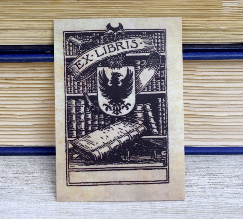 K&ouml;nnte beinhalten: Ein Exlibris im Vintage-Stil mit einer Schwarzwei&szlig;illustration eines B&uuml;cherregals, eines Adlers und eines Buches. Der Text "Ex Libris" ist auf einem Banner &uuml;ber dem Adler geschrieben.