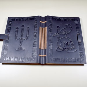 Photograph of a black leather journal, open and face down on a table, showing the embossed designs on front and back covers