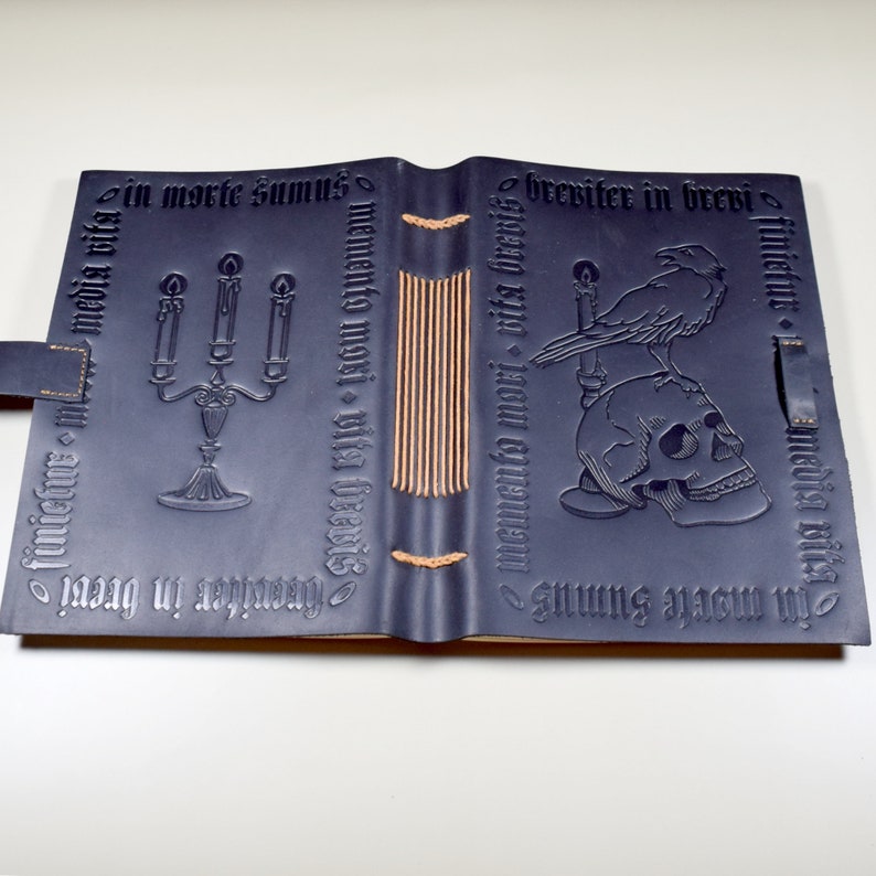 Photograph of a black leather journal, open and face down on a table, showing the embossed designs on front and back covers