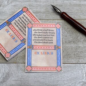 Pode incluir: Dois ex libris com uma borda azul e vermelha e um fundo creme. O texto no ex libris diz "who folds a leaf down the devil make brown who makes markorbloc the devil coasts hot whosteals this book the devil shall cook EX LIBRIS".