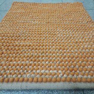 May include: Rectangular orange and beige rug with a textured, dotted pattern. The rug has a border of orange dots and a beige base. The rug is made of a woven material.