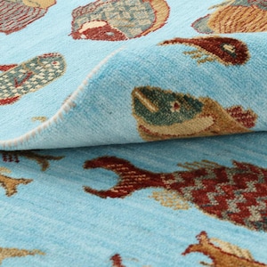 Könnte beinhalten: Hellblauer Teppich mit einem sich wiederholenden Muster aus bunten Fischen. Die Fische sind in Braun-, Rot- und Grüntönen gehalten und weisen detaillierte Schuppen und Flossen auf. Der Teppich ist gerollt und zeigt seine Textur.