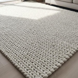 以下が含まれることがあります： 太い織り目模様の、長方形のライトグレーの大きなラグ。厚くて柔らかい素材で作られており、シンプルでモダンなデザインです。木製の床に置かれており、ソファと窓の近くにあります。