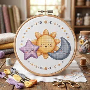 May include: A cross-stitch embroidery hoop featuring a smiling sun, star, and moon design. The embroidery is in yellow, purple, and blue, surrounded by stars and moons. The wooden hoop is displayed on a wooden table with embroidery floss and scissors.