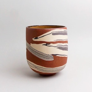 Pode incluir: Uma caneca de cerâmica branca com uma alça preta e o texto "But First, Coffee" em negrito preto. A caneca está sobre uma superfície de madeira. A caneca tem aproximadamente 10 cm de altura.