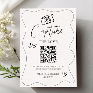 May include: A white card with black script and a QR code. The words "Capture the Love" are above the code, with a camera icon. Below the code, it says "Share your photos with us! Just scan the QR code." The names "Olivia & Henry" and the date "04.12.26" are at the bottom.