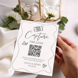 May include: A cream-colored card with the words "Capture the Love" and a QR code. The card also includes the names "Olivia & Henry" and the date "04.12.26". The card is decorated with a camera icon and heart symbols.